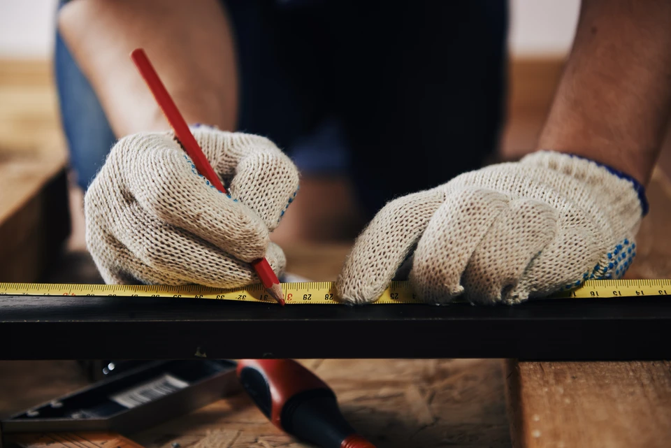 Gros plan sur des mains d'artisans avec des gants mesurant une planche en bois avec une règle et un crayon