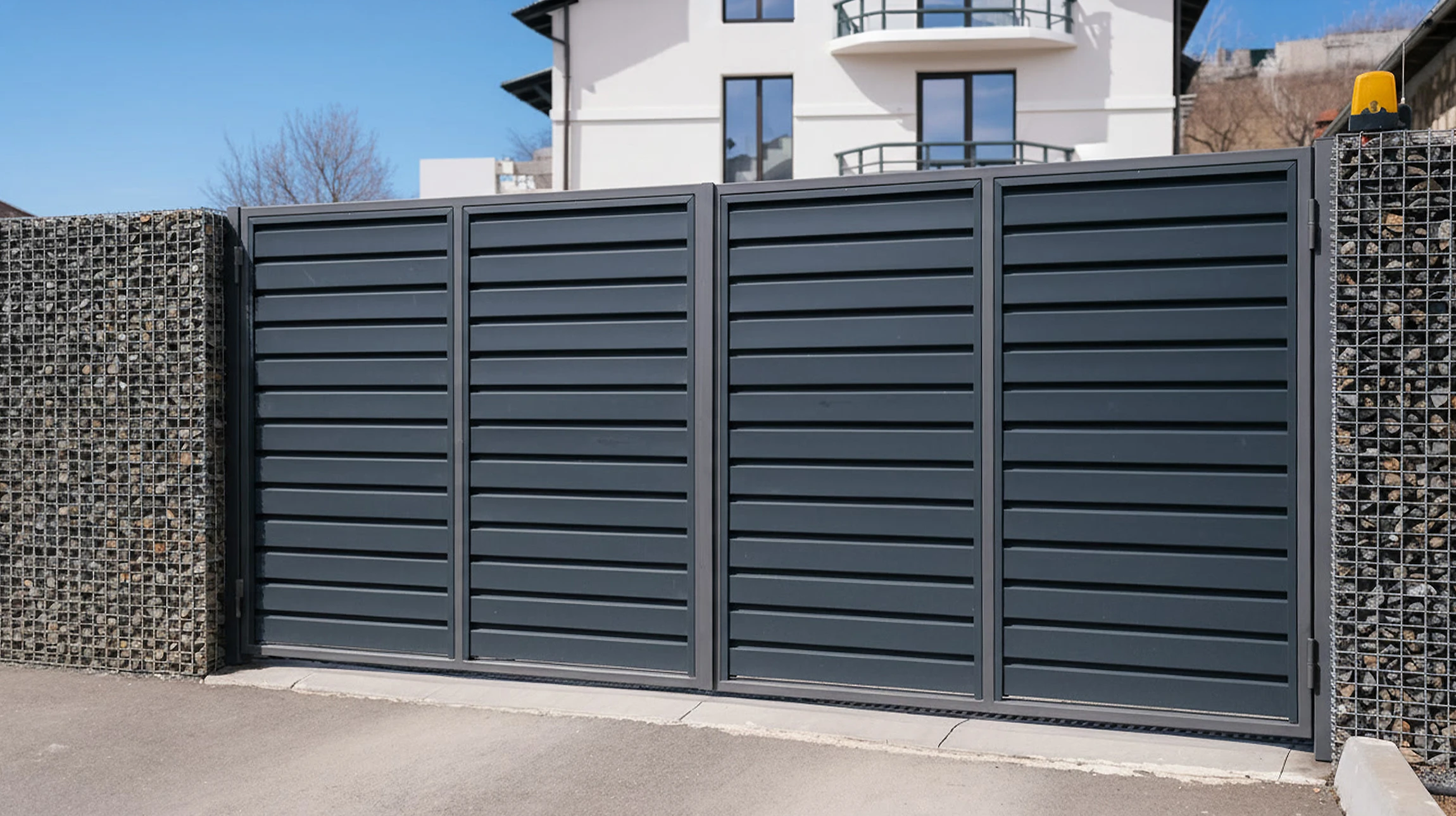 Entrée contemporaine d'une maison moderne avec porte d'entrée en bois et verre, pilier en pierre naturelle, revêtement horizontal gris, paillasson bleu marine sur dalle béton polie