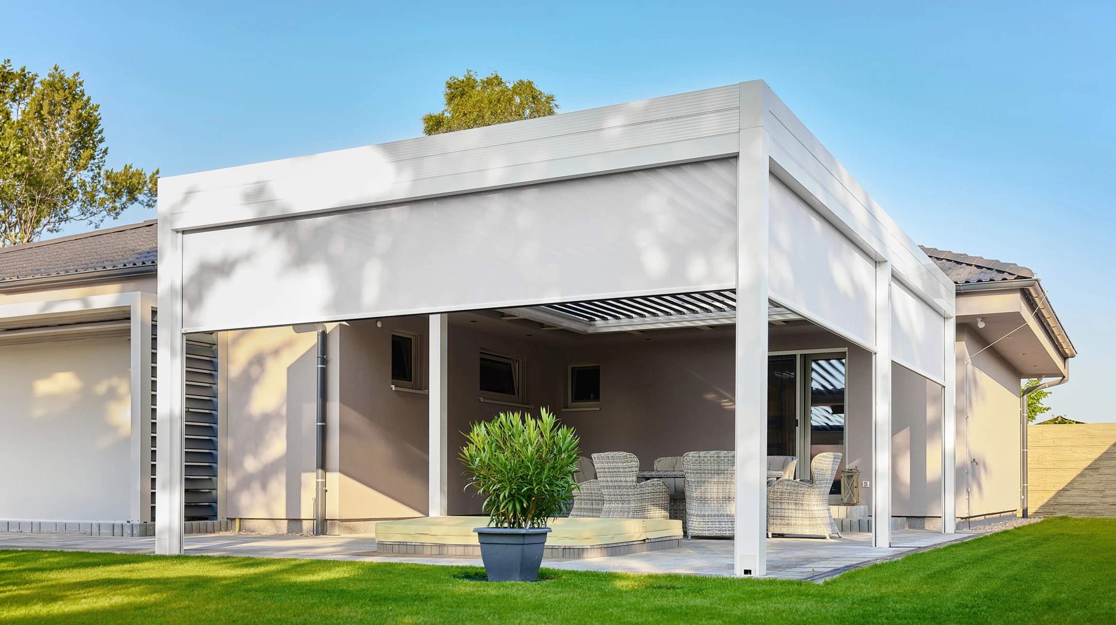 Maison individuelle moderne avec véranda vitrée attenante, jardin paysagé avec pelouse entretenue et massifs d'arbustes