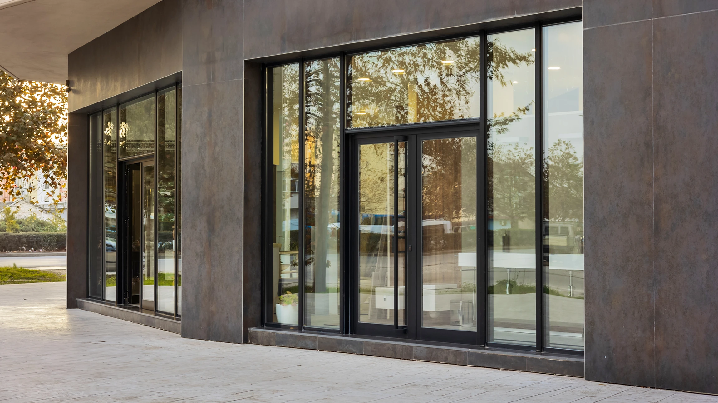 Jeune femme souriante en tablier noir et t-shirt blanc, bras croisés, debout devant l'entrée vitrée de son commerce